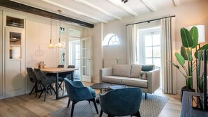 A modern living room with a sofa, two chairs, a dining table, and a large window. - Seals Cozy Farm Stay (De Cocksdorp Texel)