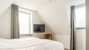 A modern bedroom with a large bed, a flat-screen TV mounted on the wall, and a window with curtains.