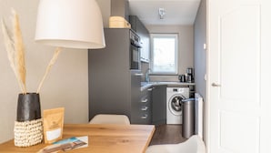 A compact kitchen with a washing machine, a coffee maker, and a window with blinds.