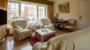 A spacious room with a large window, a wooden desk, two armchairs, a sofa, and a television. - Nice holiday home in Ostend by the sea with a terrace (Oostende)