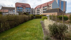 A residential building with multiple balconies, a well-maintained lawn, and a modern high-rise structure in the background. - Nice holiday home in Ostend by the sea with a terrace (Oostende)