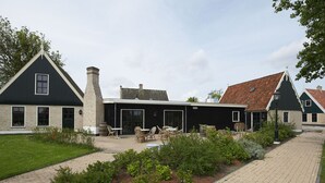 Een traditioneel gebouw met een zwarte gevel, een schoorsteen en een overdekt terras met tafels en stoelen.
