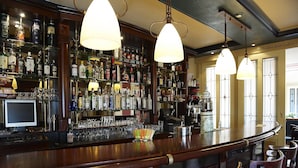 Een bar met verschillende drankflessen, glazen en een kassa.