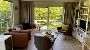 Een moderne woonkamer met een bruine bank, een grijze fauteuil, een kleine ronde tafel en een boekenkast vol boeken.