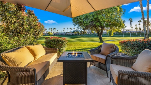 Un patio al aire libre con mobiliario de mimbre, una chimenea y vistas a un campo de golf.
