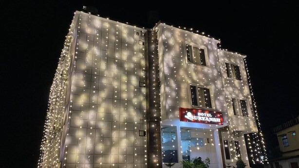 Een hotelgebouw met een bord waarop 'Hotel Suryansh' staat, verlicht door talloze lichten in de nacht.
