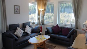 A living room with two black sofas, a wooden coffee table, and a lamp. There are windows with curtains, a framed picture on the wall, and a vase with flowers on a table. - Apartment in Willingen mit Balkon (Willingen)