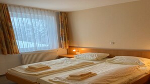 A double bed with white linens and towels, a bedside table with a lamp, a window with sheer curtains, and a radiator. - Apartment in Willingen mit Balkon (Willingen)