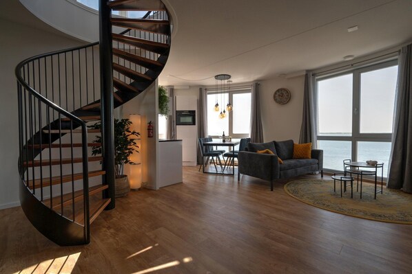 A modern living room with a spiral staircase, a dining area, and a large window with a view.