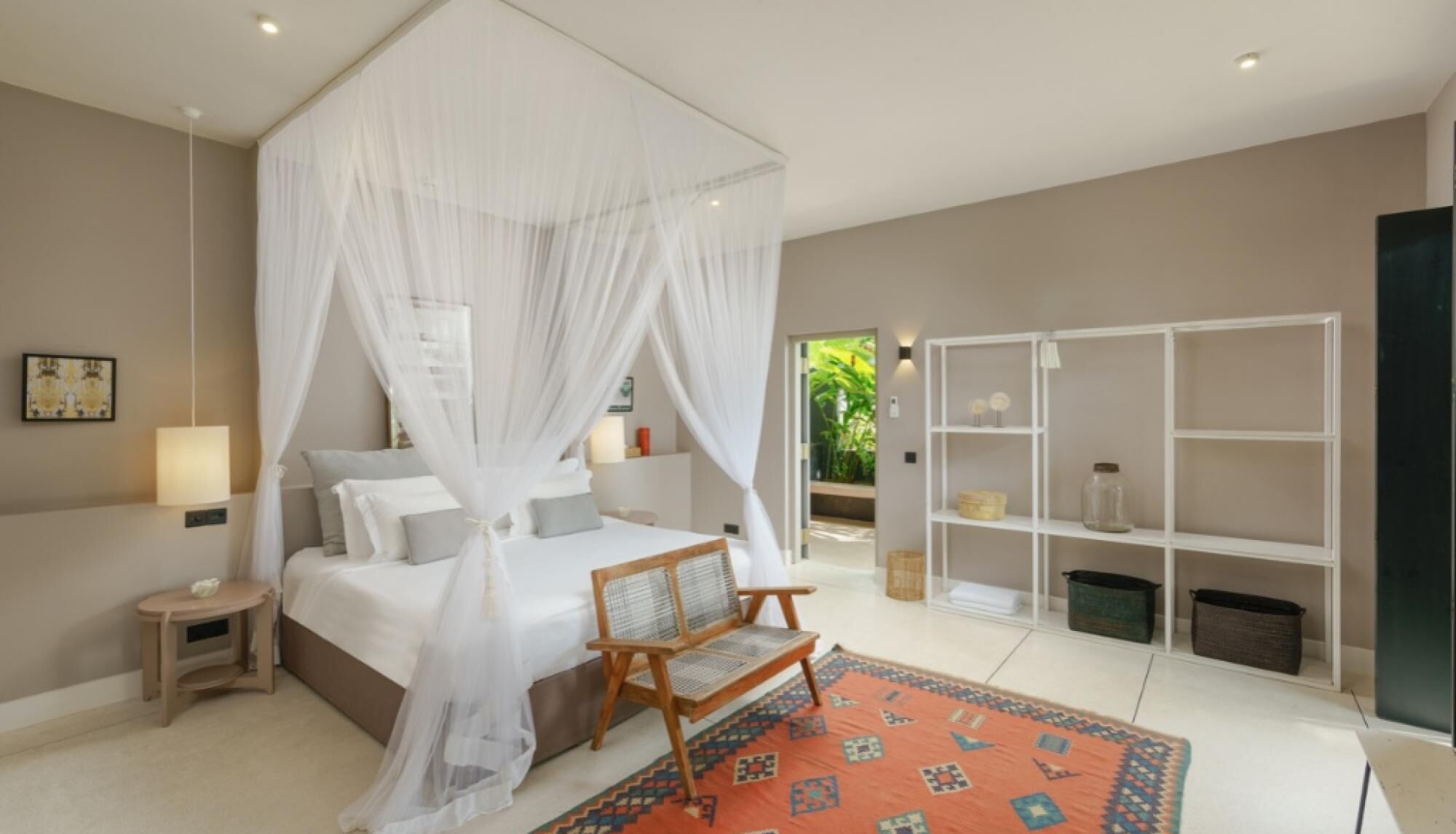 A bedroom with a four-poster bed, a wooden chair, a bookshelf, and a view of greenery outside.