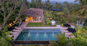 Un espace piscine avec une maison, le tout entouré d’une végétation luxuriante et de palmiers.