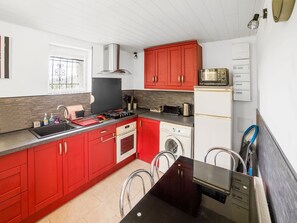 Une cuisine compacte avec des meubles rouges, une hotte en acier inoxydable, un four à micro-ondes, un grille-pain et un lave-linge.