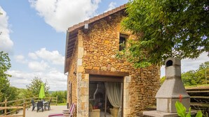 Un bâtiment en pierre doté d’une cheminée, d’un espace extérieur aménagé pour s’asseoir et d’une terrasse en gravier.