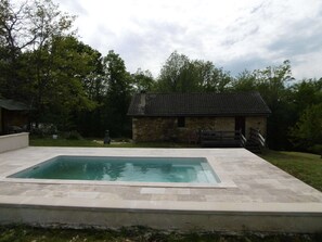 Une piscine rectangulaire bordée de pierres, entourée d’une pelouse et d’un bâtiment en pierre doté d’un toit en tuiles.