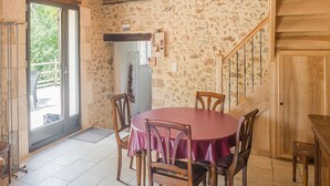 Un coin repas avec une table ronde et quatre chaises, un escalier en bois et un mur en pierre.