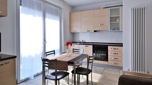 A modern kitchen with a dining area, featuring sliding glass doors, light wood cabinets, and a black countertop. - Apartment by Lake Como with Scenic Views (Dervio)