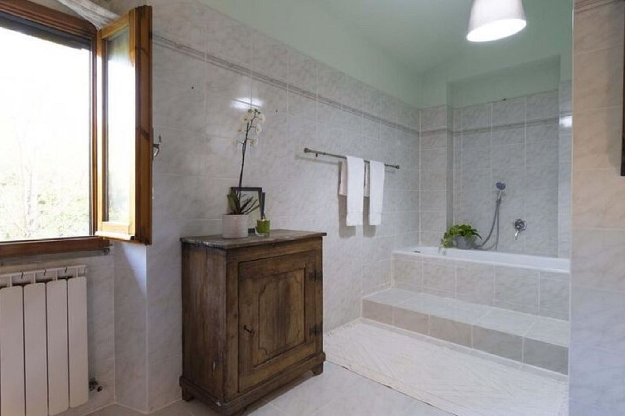 A bathroom with a bathtub, a wooden cabinet, a window, and a towel rack.