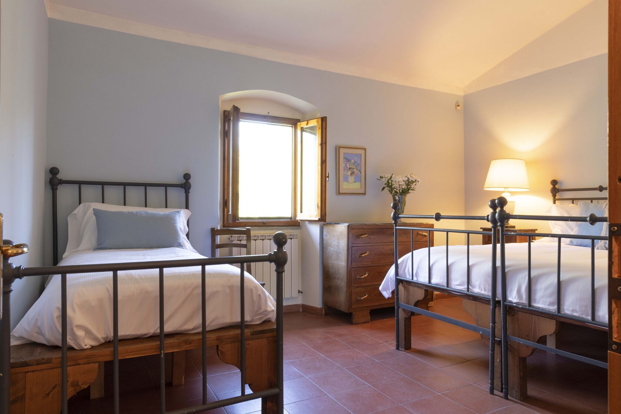 Una camera da letto con due letti, una cassettiera, una finestra e una lampada.