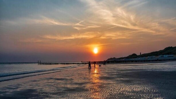 Une plage au coucher du soleil, avec une jetée qui s’avance dans l’eau.