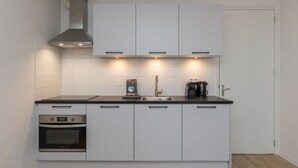 Une cuisine moderne avec des armoires blanches, un four encastré, une hotte de cuisinière en acier inoxydable et un plan de travail noir.