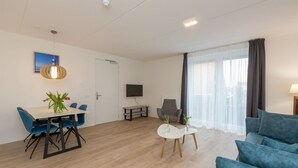 Un salon moderne comprenant un coin repas, un téléviseur à écran plat et une grande fenêtre avec des rideaux.