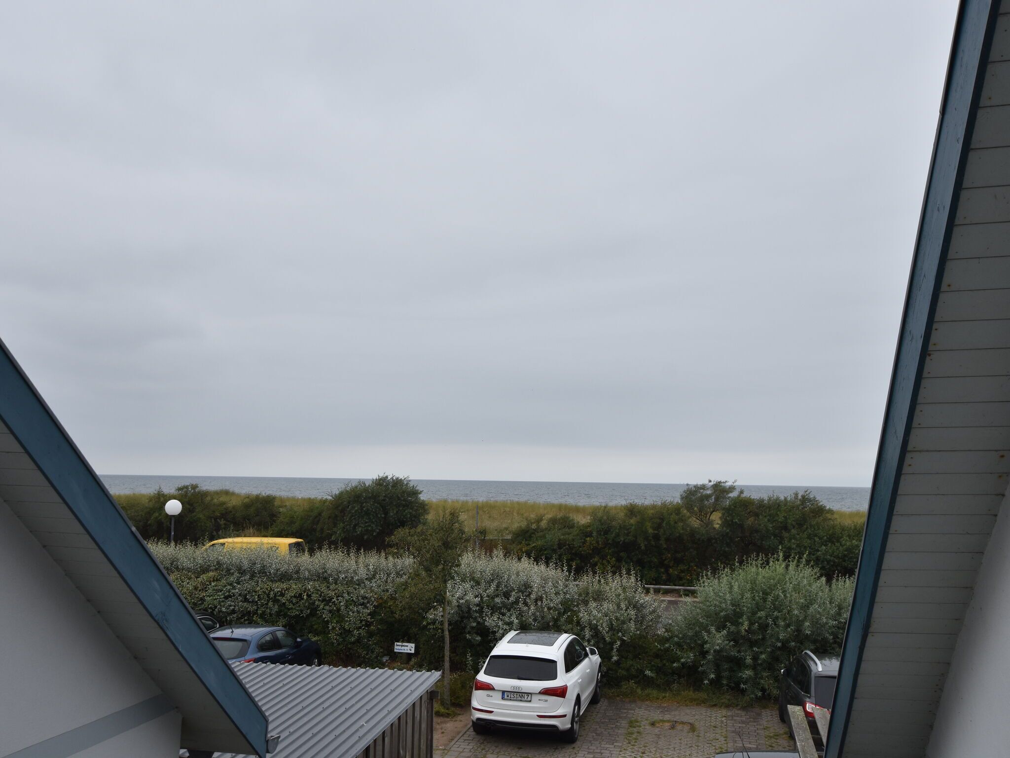 Blick aus einem Fenster auf einen Parkplatz, vor dem ein weißes Auto steht.