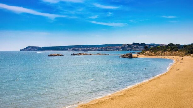 Una platja amb aigua blava i transparent, sorra daurada i roques.
