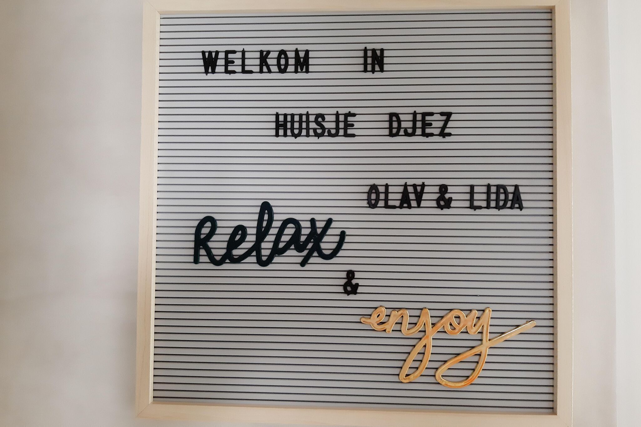 A framed welcome sign with the text "WELCOME IN HUISJE DJEZ OLAV & LIDA Relax & enjoy".