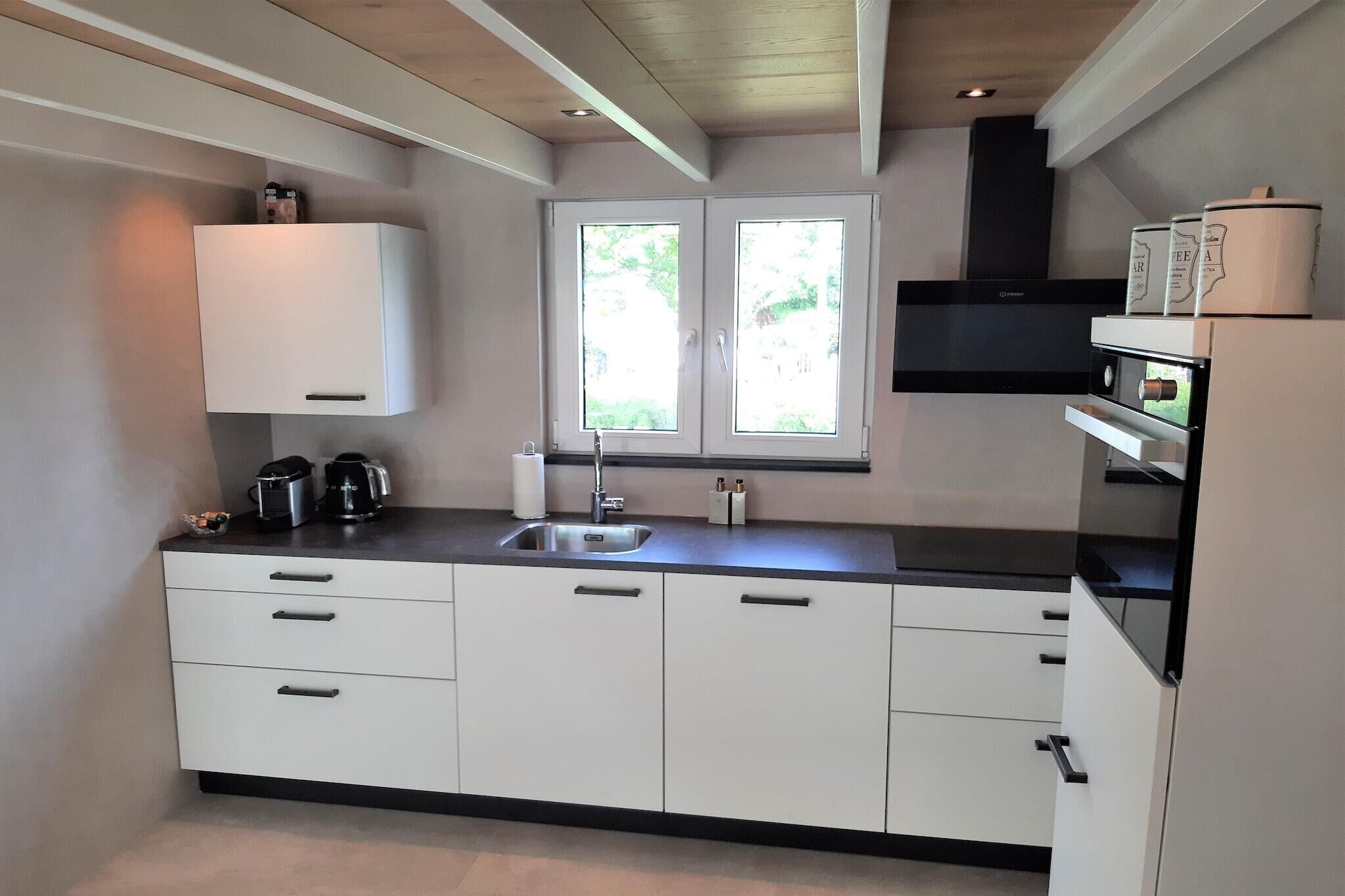 A modern kitchen with white cabinets, a black countertop, a built-in oven, and a window with a view of greenery outside.