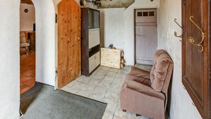 Una habitación acogedora con una puerta de madera, un pequeño armario de madera, un sillón acolchado y un piso de baldosas.