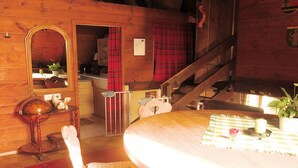 A wooden interior with a round dining table, a chair, a mirror, a staircase, and a small table with a globe and a plant.