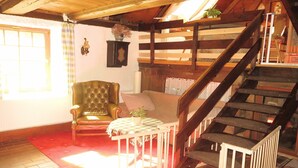 A cozy room with a wooden staircase, a green armchair, a white table with a checkered tablecloth, and a red carpet.
