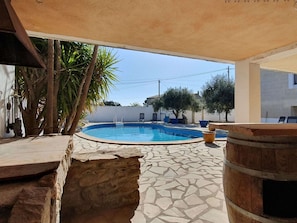 Una piscina con baldosas de piedra, un barril de madera y una zona de estar cubierta.