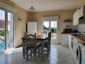 A kitchen with a dining table, chairs, a refrigerator, a washing machine, and a view of a swimming pool. - Majestic Villa in Homps with Private Pool (Homps)
