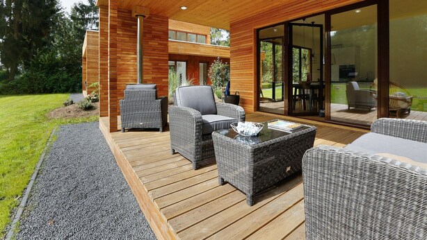 Une terrasse extérieure moderne, dotée de meubles en osier, d’une porte vitrée donnant sur un patio et d’un plafond en bois.
