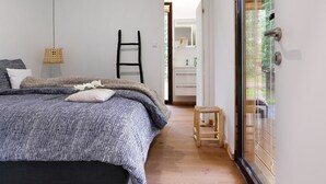 Une chambre à coucher avec un lit, une échelle, un petit tabouret et une salle de bain visible à travers une porte ouverte.