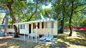 A small, single-story cabin with a porch, outdoor seating area, and a covered patio. - Caravan Park Belvedere, Grado (Belvedere di Aquileia)