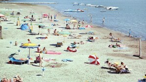 A beach with numerous umbrellas and sun loungers, boats in the water, and a clear sky. - Belvedere AC Flat in Grado Resort (Belvedere di Aquileia)