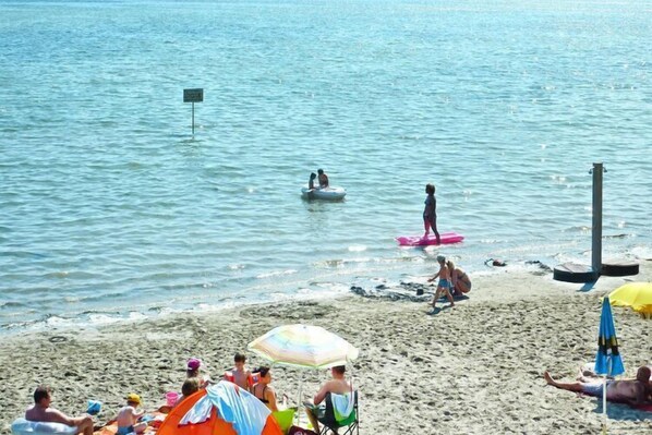Una playa con gente tomando el sol, nadando y jugando.