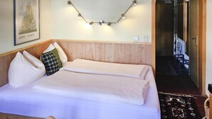Habitación de hotel con cabecera de madera, cama con ropa de cama blanca, lámpara de pared y un cuadro en la pared.