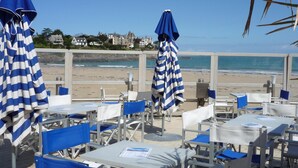 Un restaurante frente a la playa con sombrillas a rayas y sillas azules, con vista al océano.