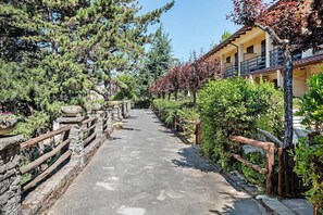 Ein gepflasterter Weg, der von Holzzäunen und dichtem Grün gesäumt wird und zu einem Gebäude mit einem Balkon führt.