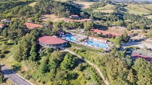 Ett flygbildsbild av ett semesterområde med en cirkelformad byggnad, flera pooler och ett omgivande skogslandskap.