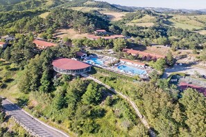 Eine Vogelperspektive zeigt ein Resort mit einem großen, runden Gebäude, mehreren Schwimmbecken und einer kurvenreichen Zufahrtsstraße.