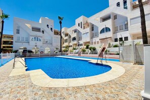 A swimming pool with a clear blue water, surrounded by a tiled deck.