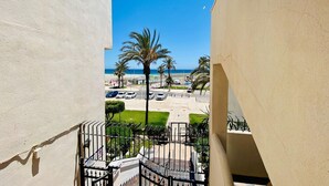 Een balkon met uitzicht op een strand, palmbomen en geparkeerde auto's.