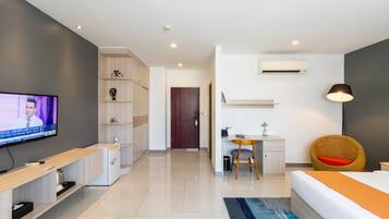 A modern hotel room with a TV, a desk, a chair, a bed, and a small kitchenette.