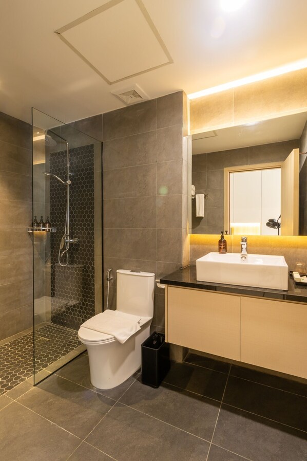 Un baño moderno con ducha envuelta en cristal, inodoro y lavabo con espejo sobre él.