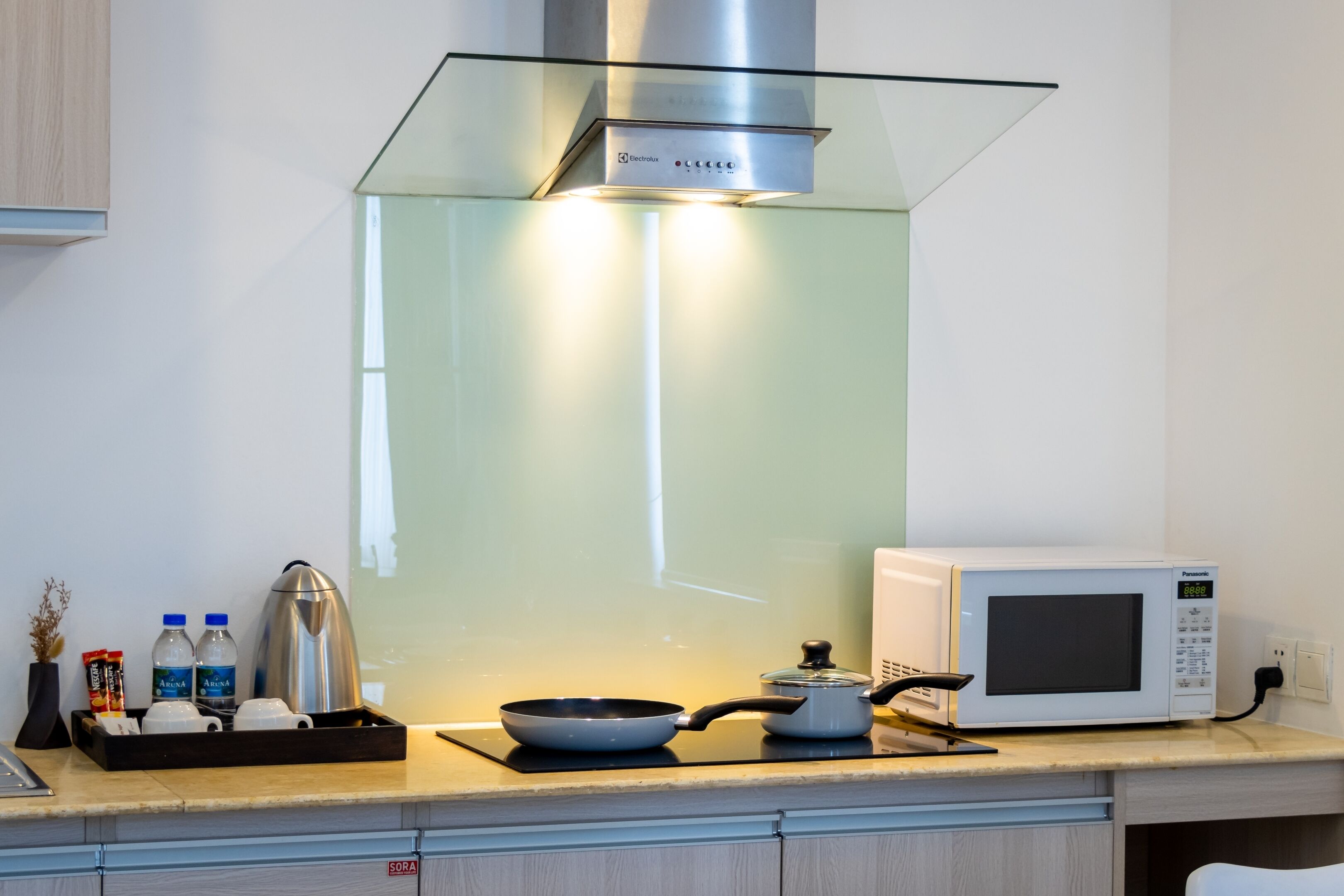 Cozinha moderna com exaustor de vidro, micro-ondas, chaleira e bandeja com garrafas de água e condimentos.