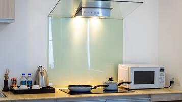 Cozinha moderna com exaustor de vidro, micro-ondas, chaleira e bandeja com garrafas de água e condimentos.
